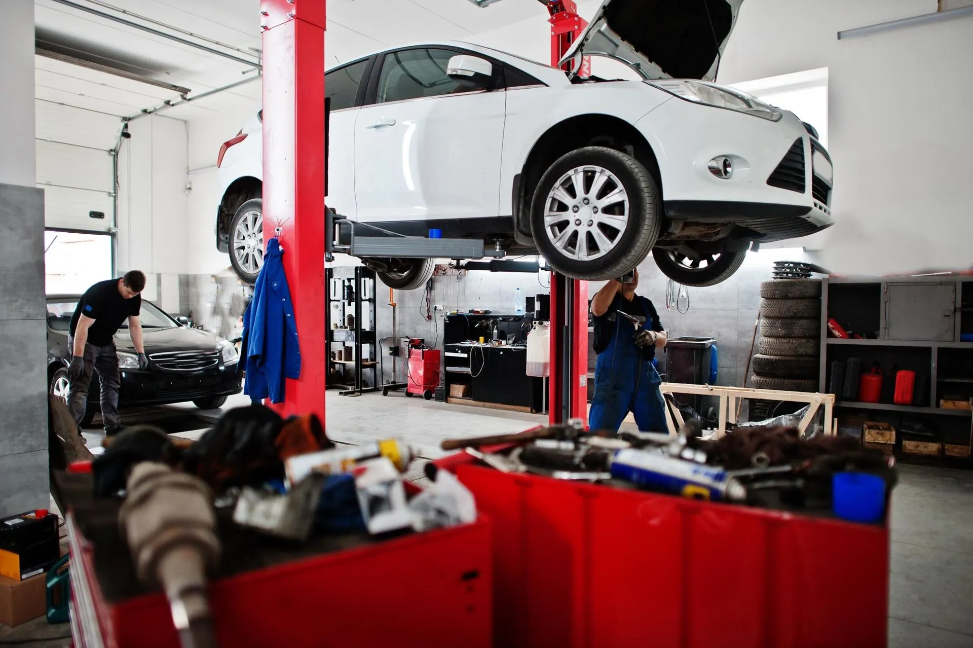 Auto auf der Hebebühne in der Werkstatthalle, zwei Mechaniker bei der Arbeit