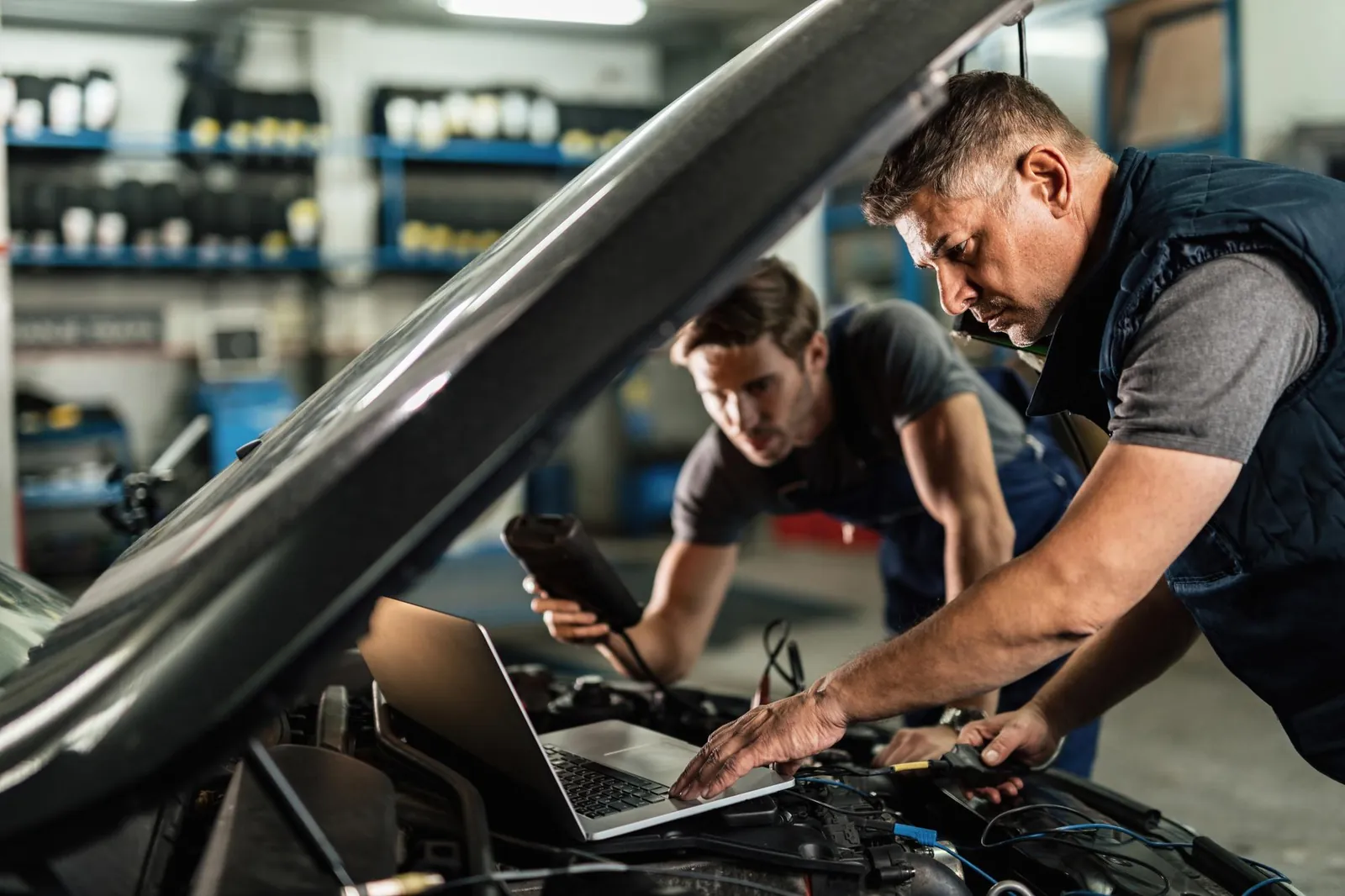 Zwei Mechaniker lesen mit Laptop und Diagnosegerät den Fehlerspeicher eines Autos aus
